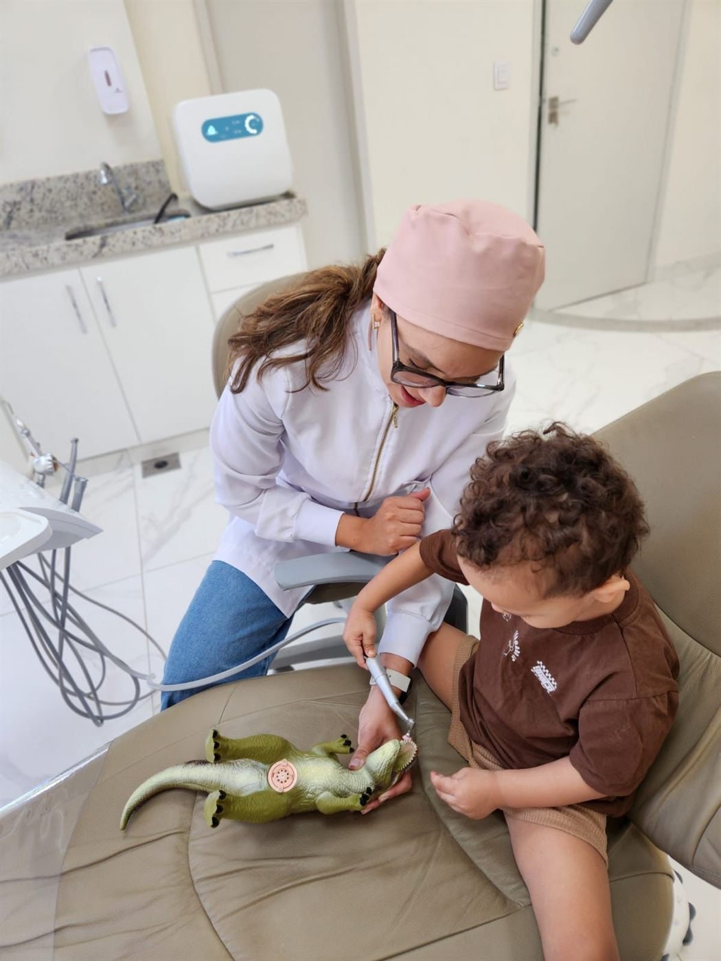 Criança na cadeira odontológica brincando com um dinossauro de brinquedo durante o atendimento.